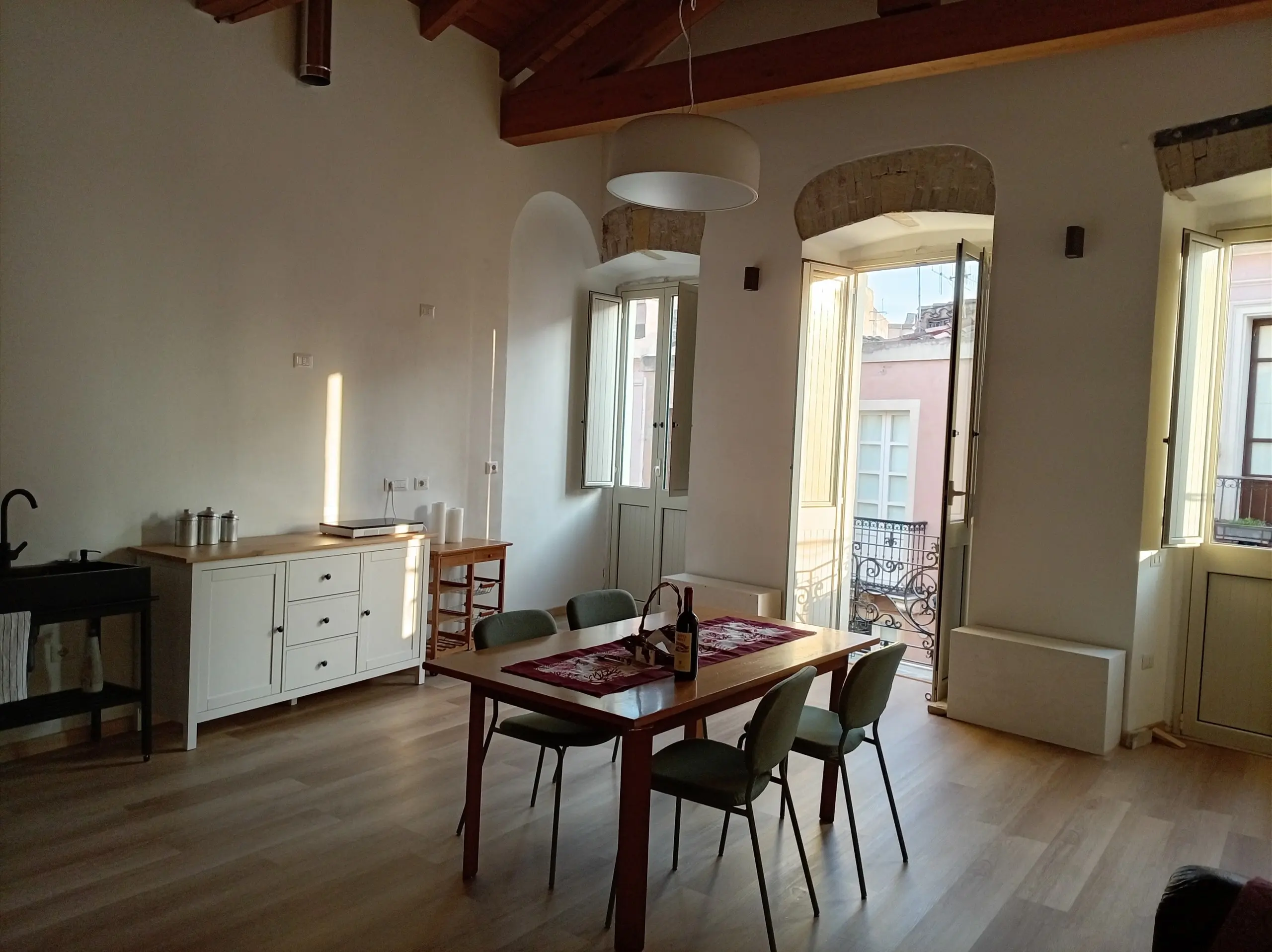 Il tavolo da pranzo sotto le travi, davanti alle due porte-finestre ad arco aperte sul centro storico